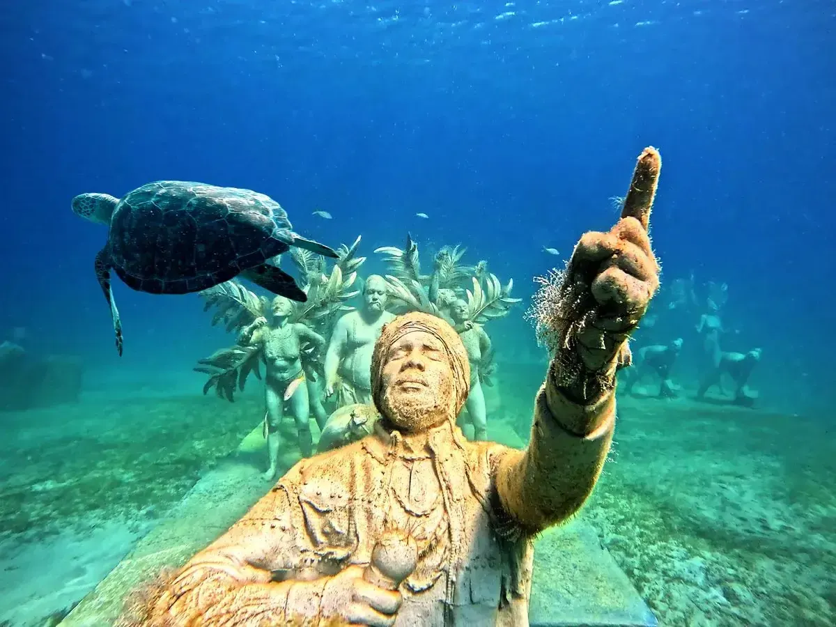 Turtle swimming above an underwater sculpture at Under SXM