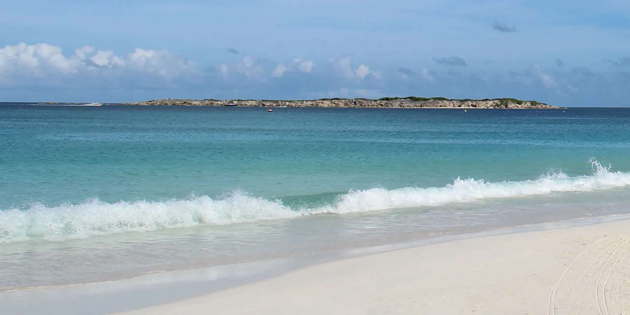 Wave breaking on the white sand of Orient Bay with Green Cay in the background