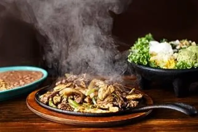 Sizzling beef fajitas served on a smoking cast-iron plate at 3 Amigos