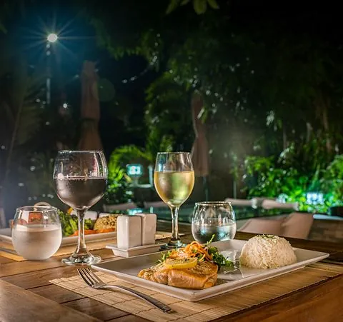 Grilled fish with rice and wine glasses on a wooden table in the 978 Sanctorum garden
