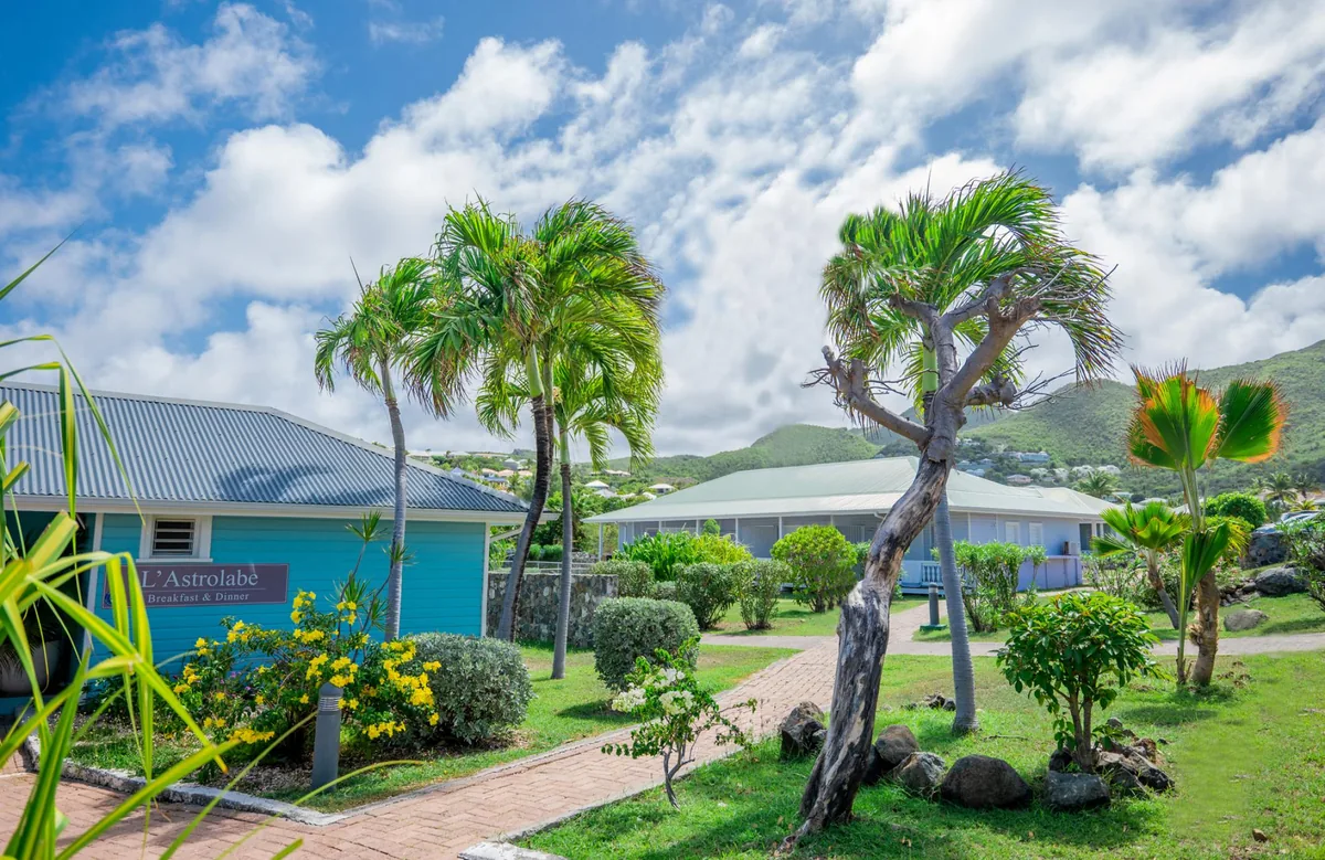 Outdoor entrance of L'Astrolabe in Orient Bay with blue sign and palm trees