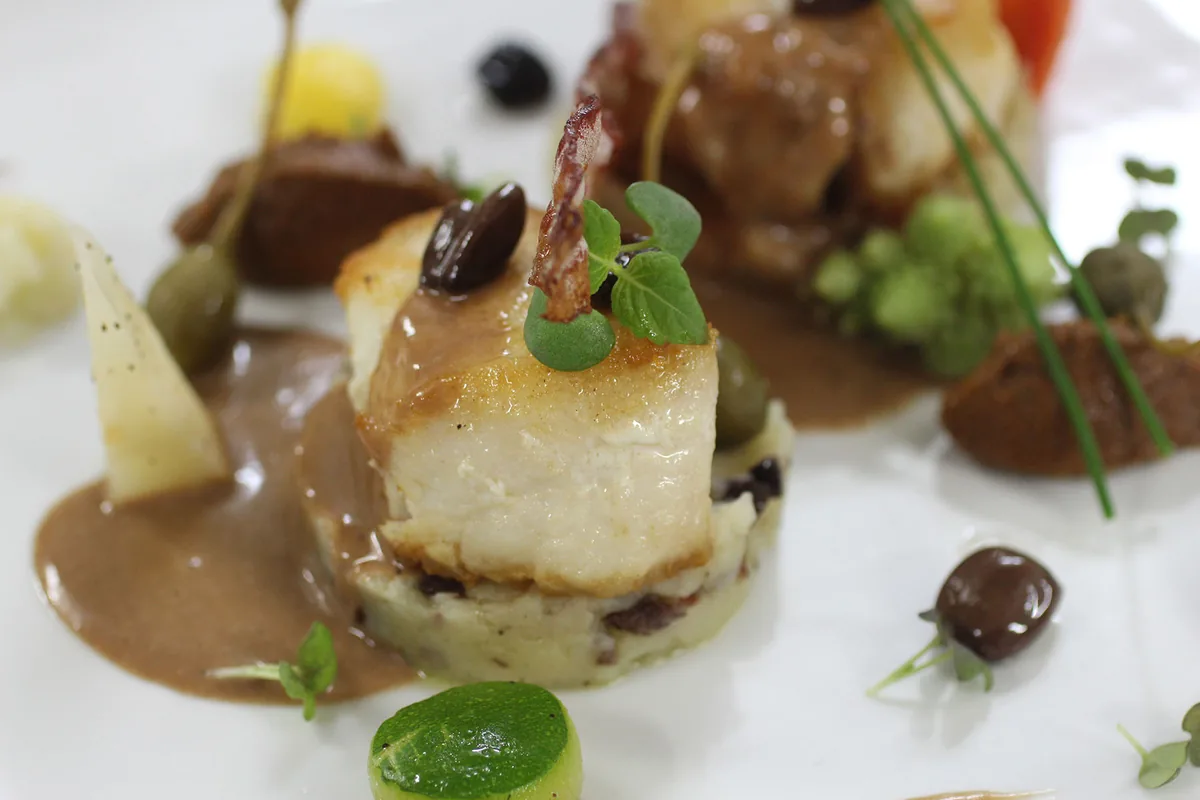 Pearly fish fillet with red wine sauce and olive purée, fine plating at L'Astrolabe