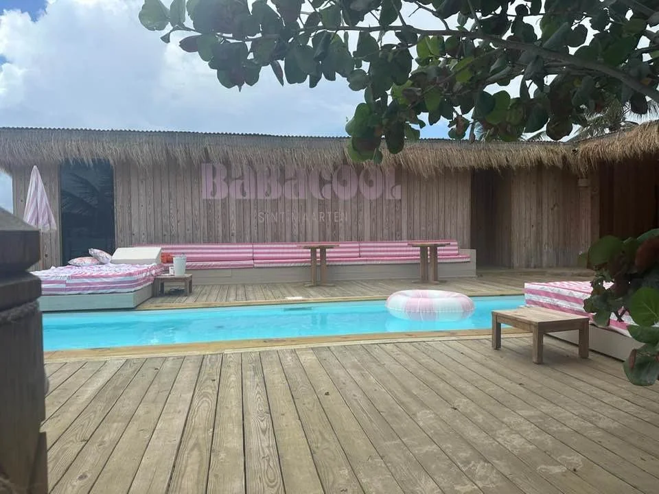 Babacool pool with pink-striped daybeds and the BABACOOL Sint Maarten wooden sign