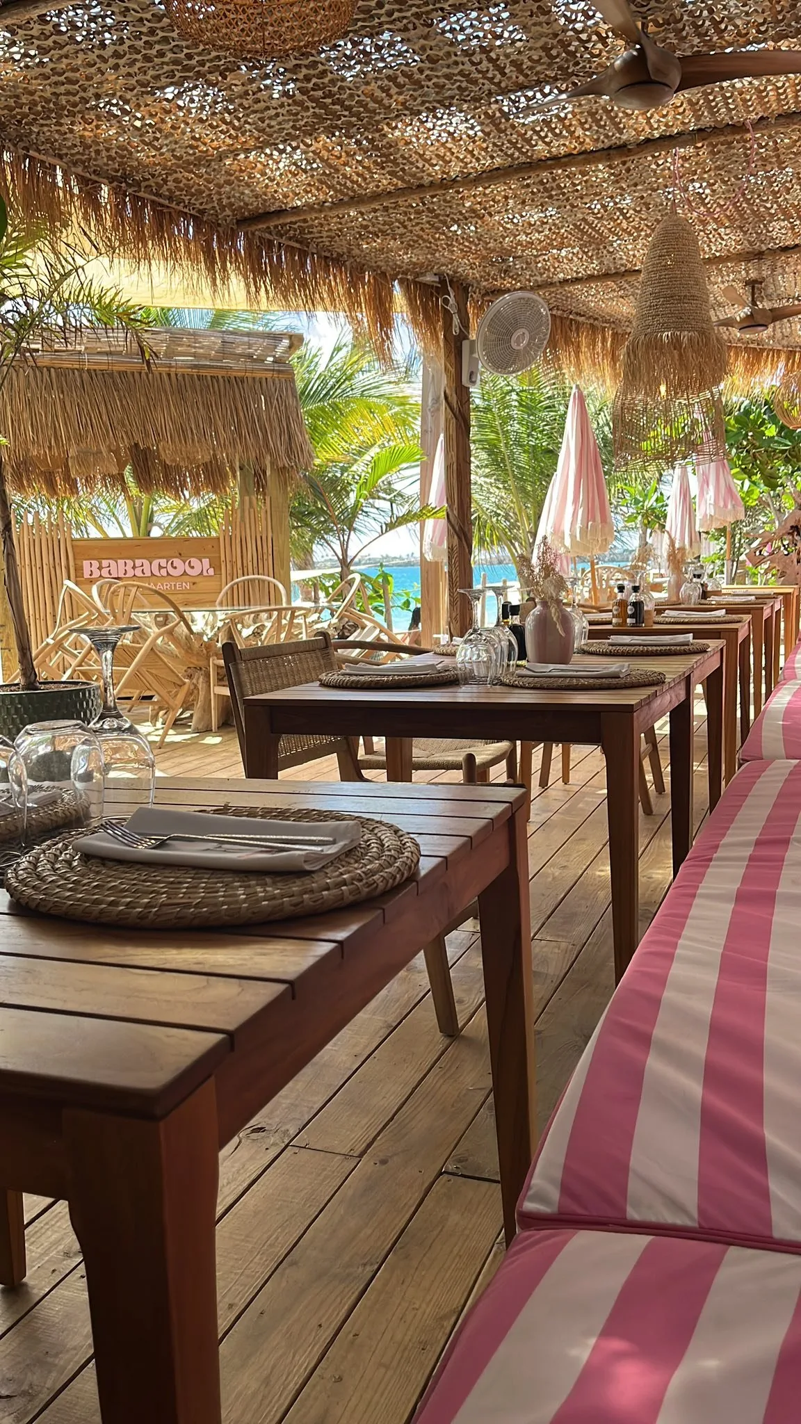 Babacool restaurant by day: wooden tables under thatched roof with the BABACOOL sign in the background