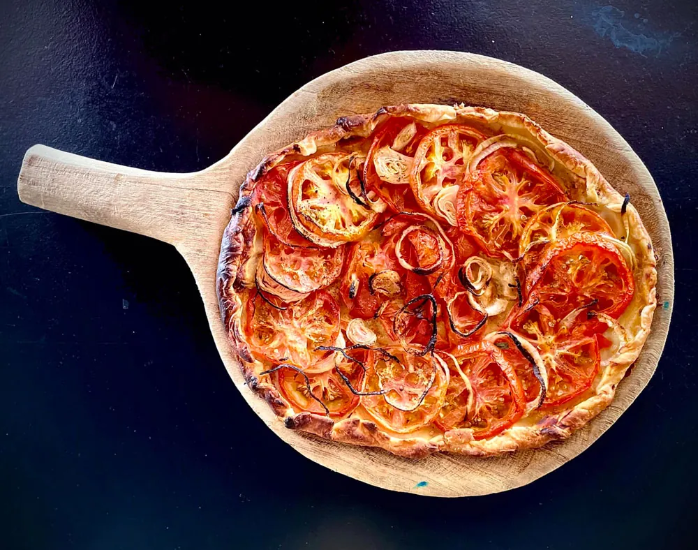 Thin tomato and onion tart served on a wooden board at Korner SXM