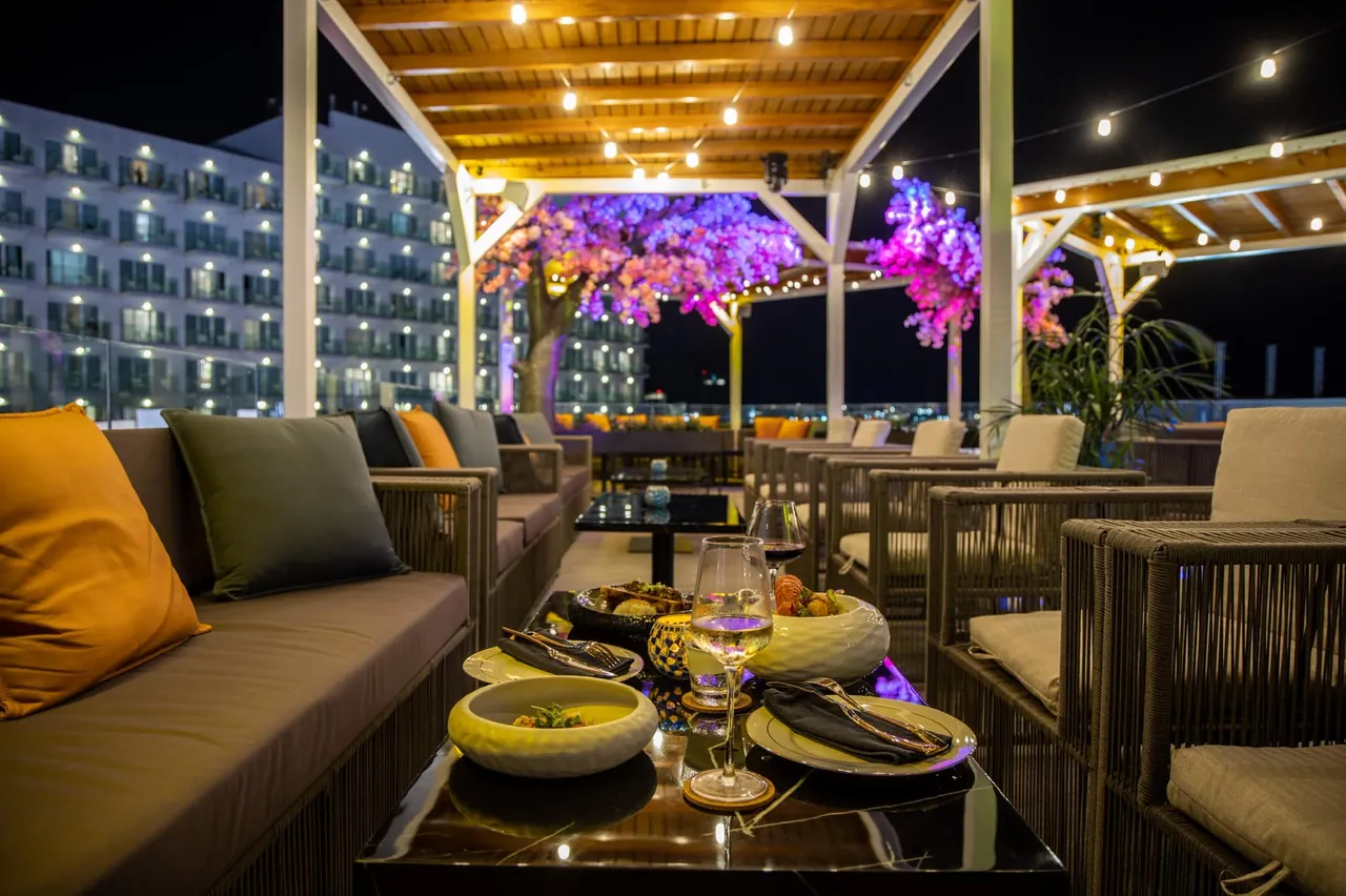 Small plates served on a low table at the Mimosa Skylounge rooftop at night