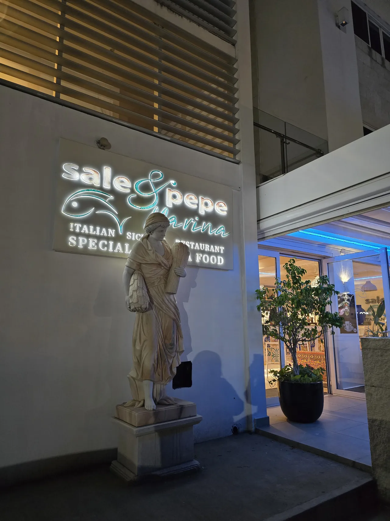 Entrance of Sale & Pepe with a Sicilian stone statue in front of the lit-up sign