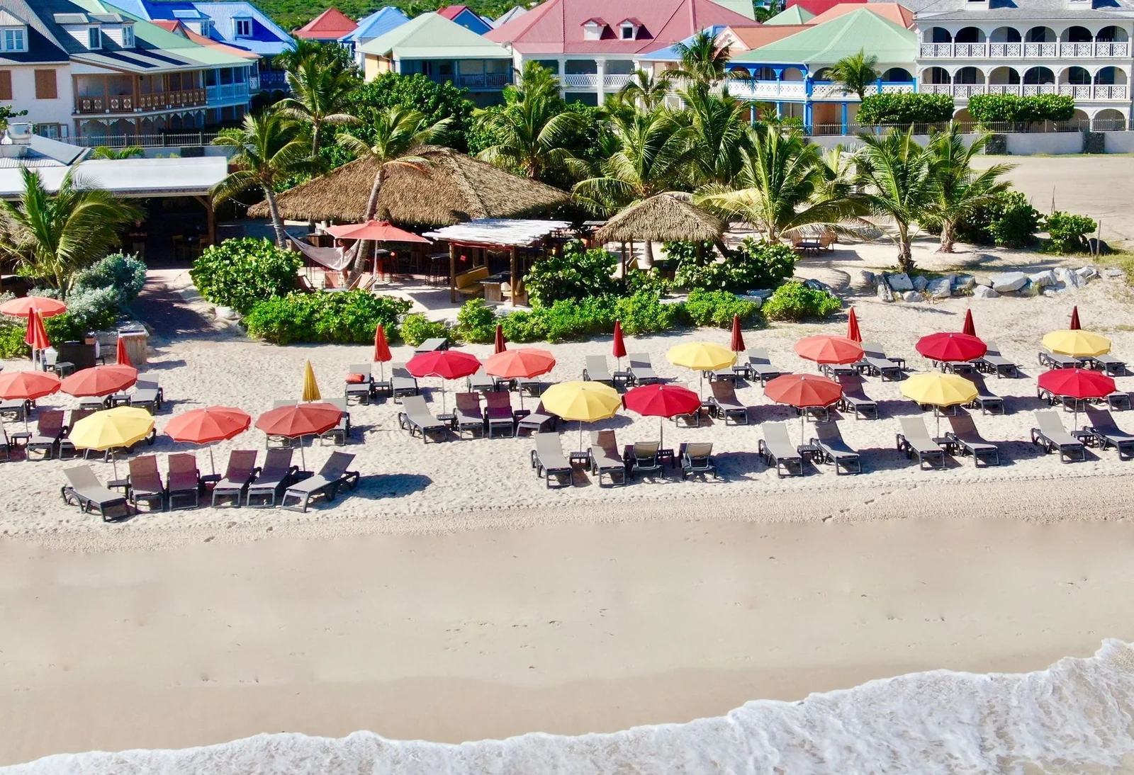 Aerial view of Waï Plage on Orient Bay with red and yellow umbrellas lined up on the white sand