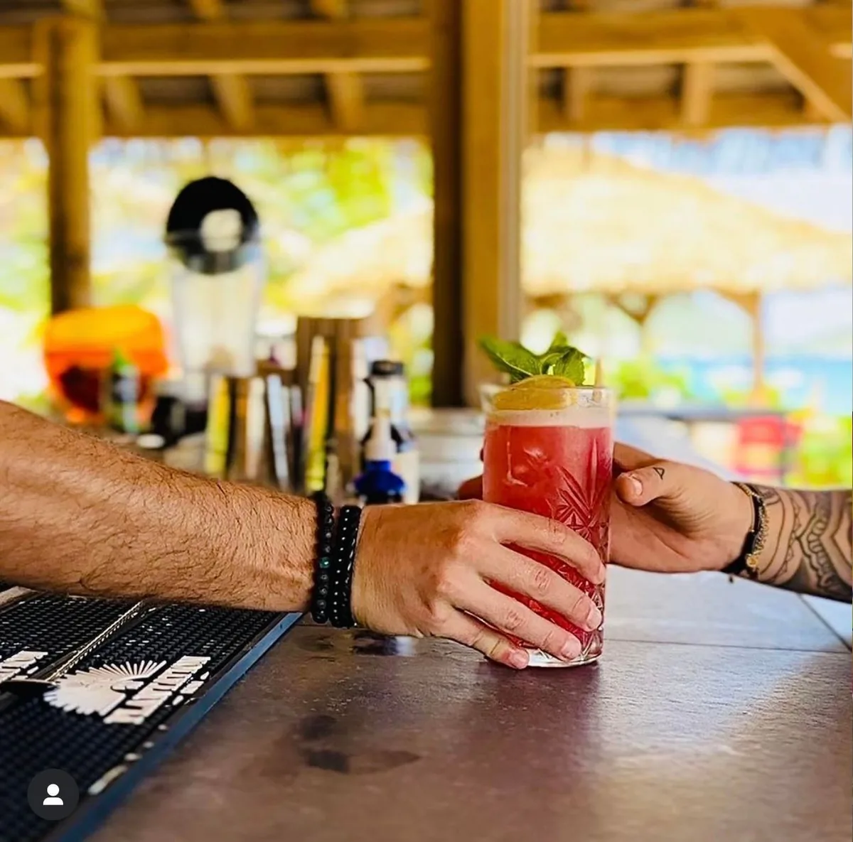 Signature cocktail being handed across the thatched beach bar at Waï Plage
