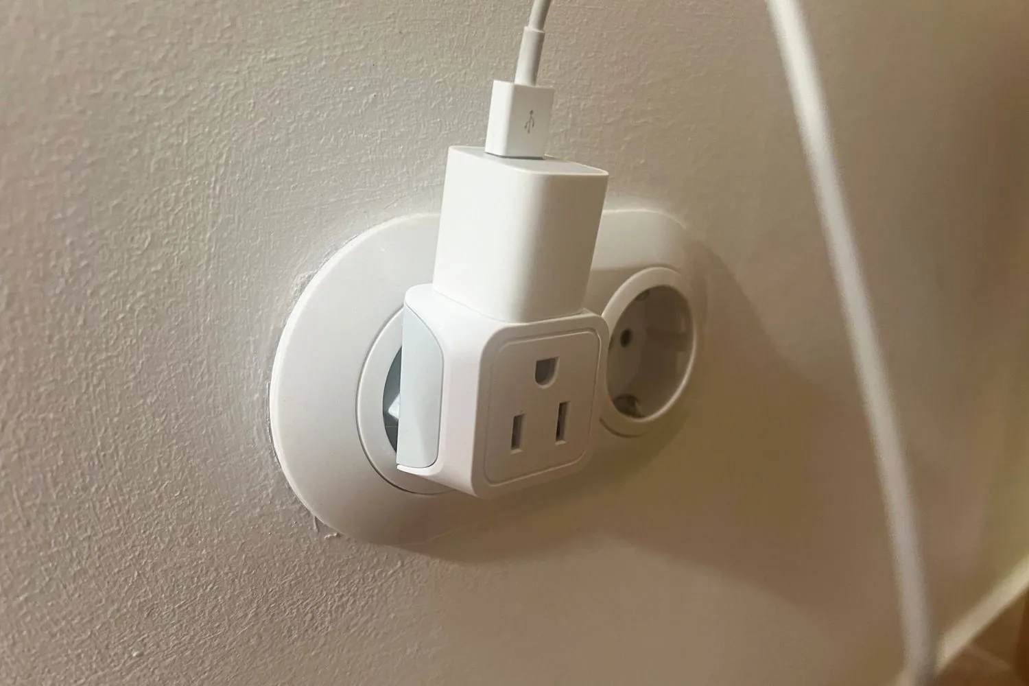 Adapter for a US plug inserted into a European wall outlet, with a phone charger
