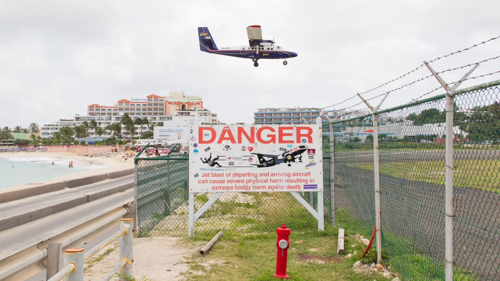 "Danger" jet blast warning sign at the end of the runway at Maho Beach, with a plane coming in to land