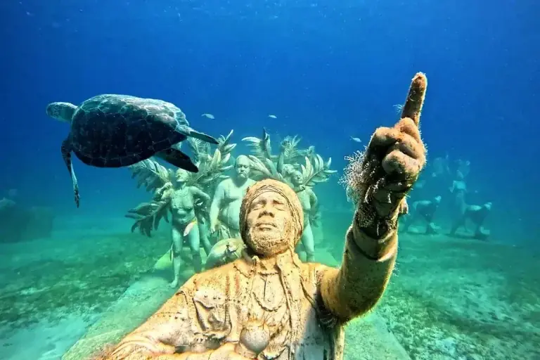 Turtle swimming above an underwater sculpture at Under SXM