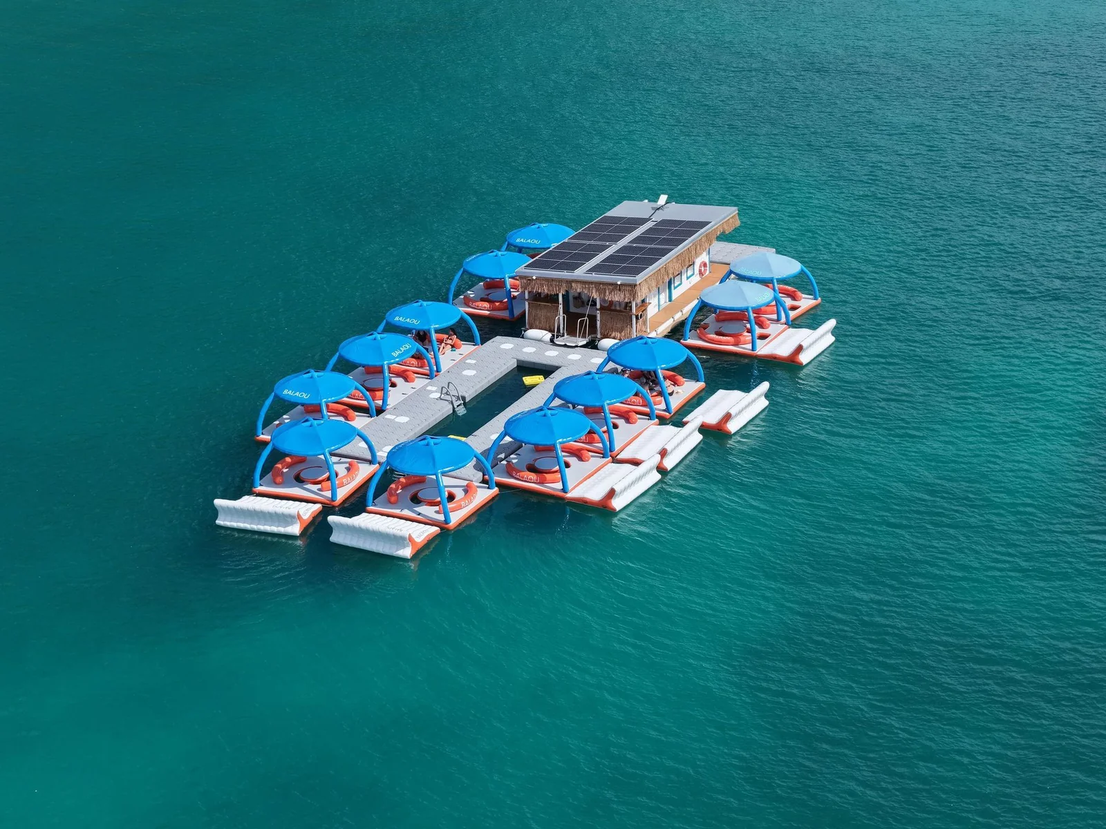 Vue aérienne du Balaou, bar-restaurant flottant avec ses salons sous parasols bleus, au milieu de l'eau turquoise de la baie de Grand Case